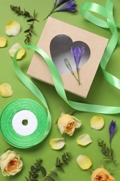 Flat lay composition with beautiful ribbon reel and gift box on green background