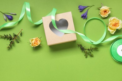 Photo of Flat lay composition with beautiful ribbon reel and gift box on green background, space for text
