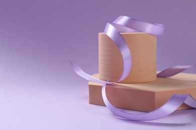 Photo of Beautiful ribbon and different podiums on violet background, space for text