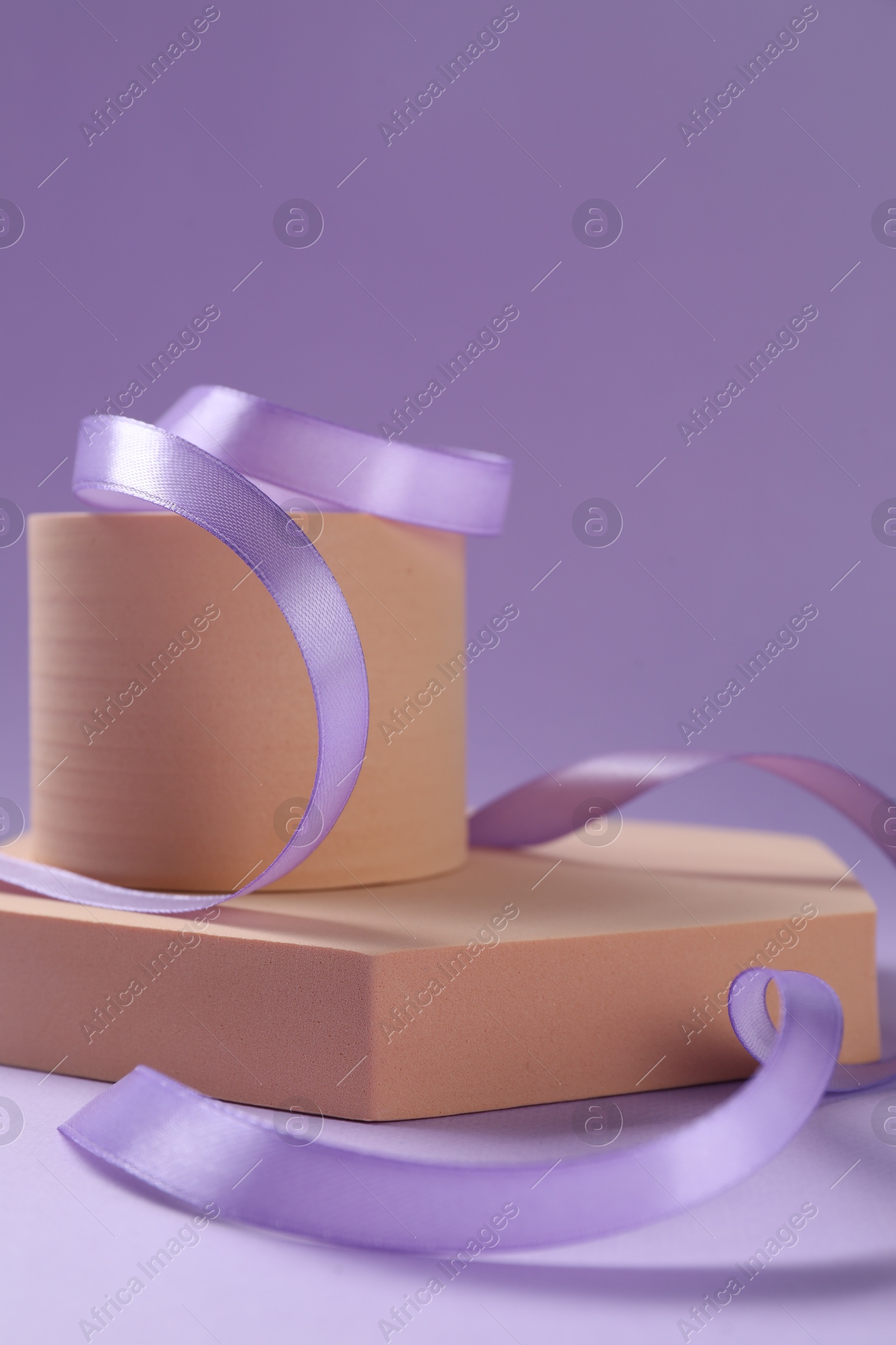 Photo of Beautiful ribbon and different podiums on violet background, closeup