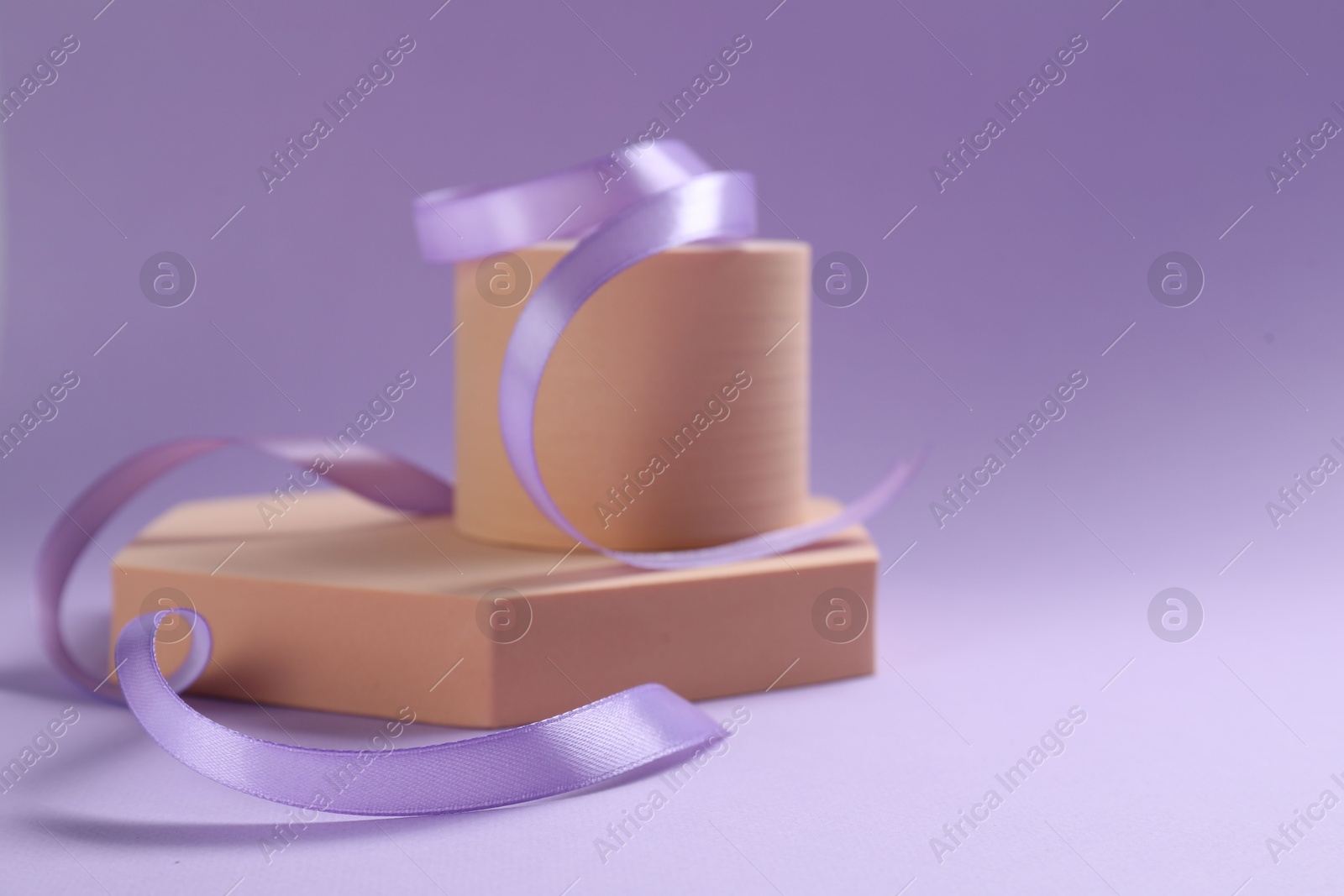 Photo of Beautiful ribbon and different podiums on violet background, closeup. Space for text