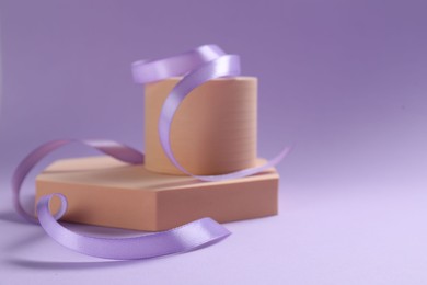 Beautiful ribbon and different podiums on violet background, closeup. Space for text