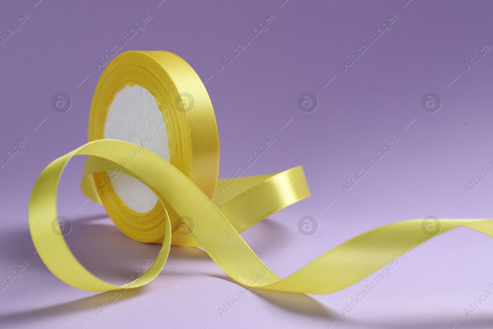Photo of Beautiful yellow ribbon reel on violet background, closeup
