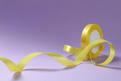 Beautiful yellow ribbon reel on violet background, closeup. Space for text