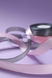 Photo of Beautiful ribbons in different colors on violet background, closeup