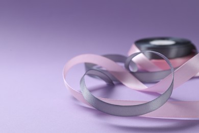 Photo of Beautiful ribbons in different colors on violet background, closeup. Space for text
