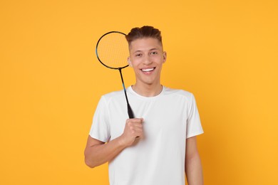 Young man with badminton racket on orange background