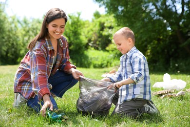 Photo of Mother and her son with plastic bag collecting garbage in park