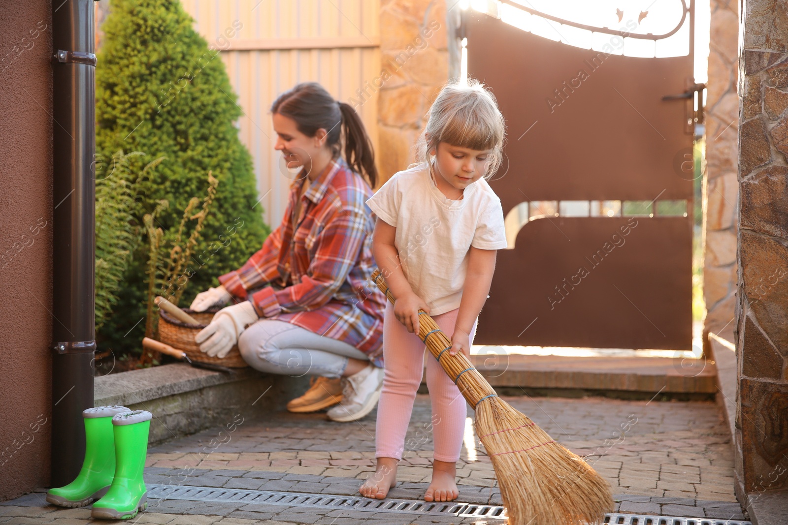 Photo of Mother and her cute daughter cleaning near house together on spring day