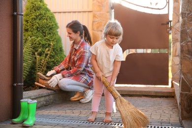 Mother and her cute daughter cleaning near house together on spring day