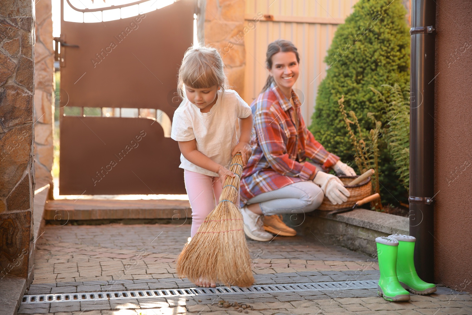 Photo of Mother and her cute daughter cleaning near house together on spring day