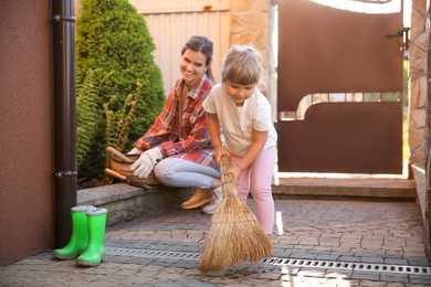 Photo of Mother and her cute daughter cleaning near house together on spring day
