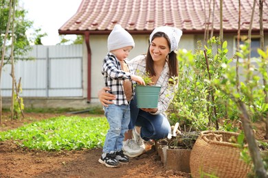 Photo of Mother and her cute son planting tree together in garden