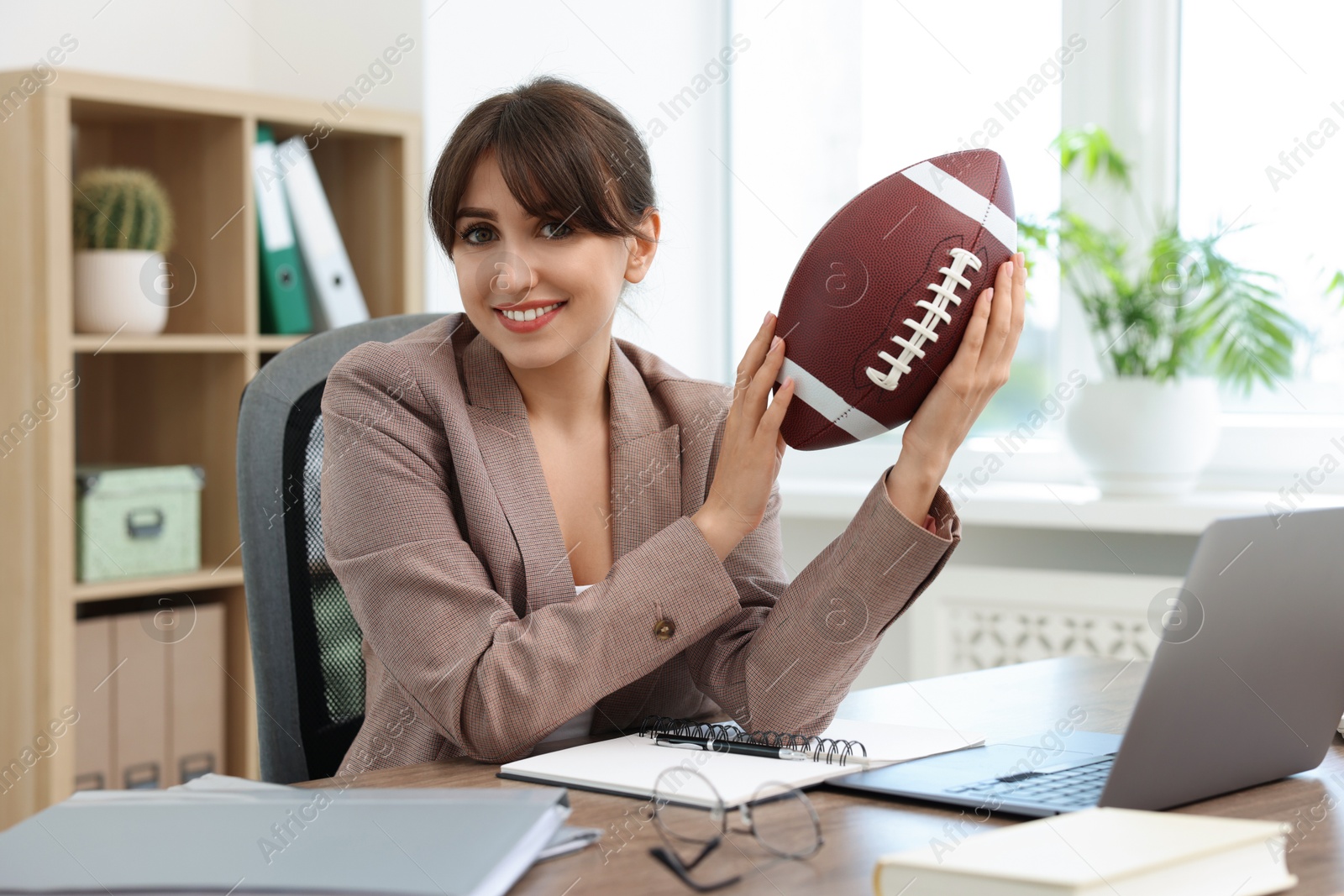 Photo of Smiling employee with american football ball at table in office