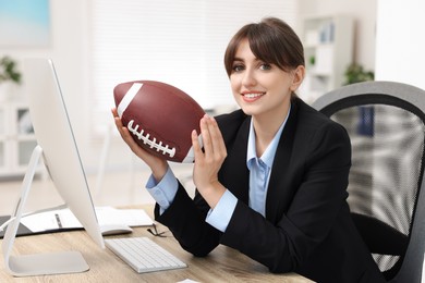 Smiling employee with american football ball at table in office