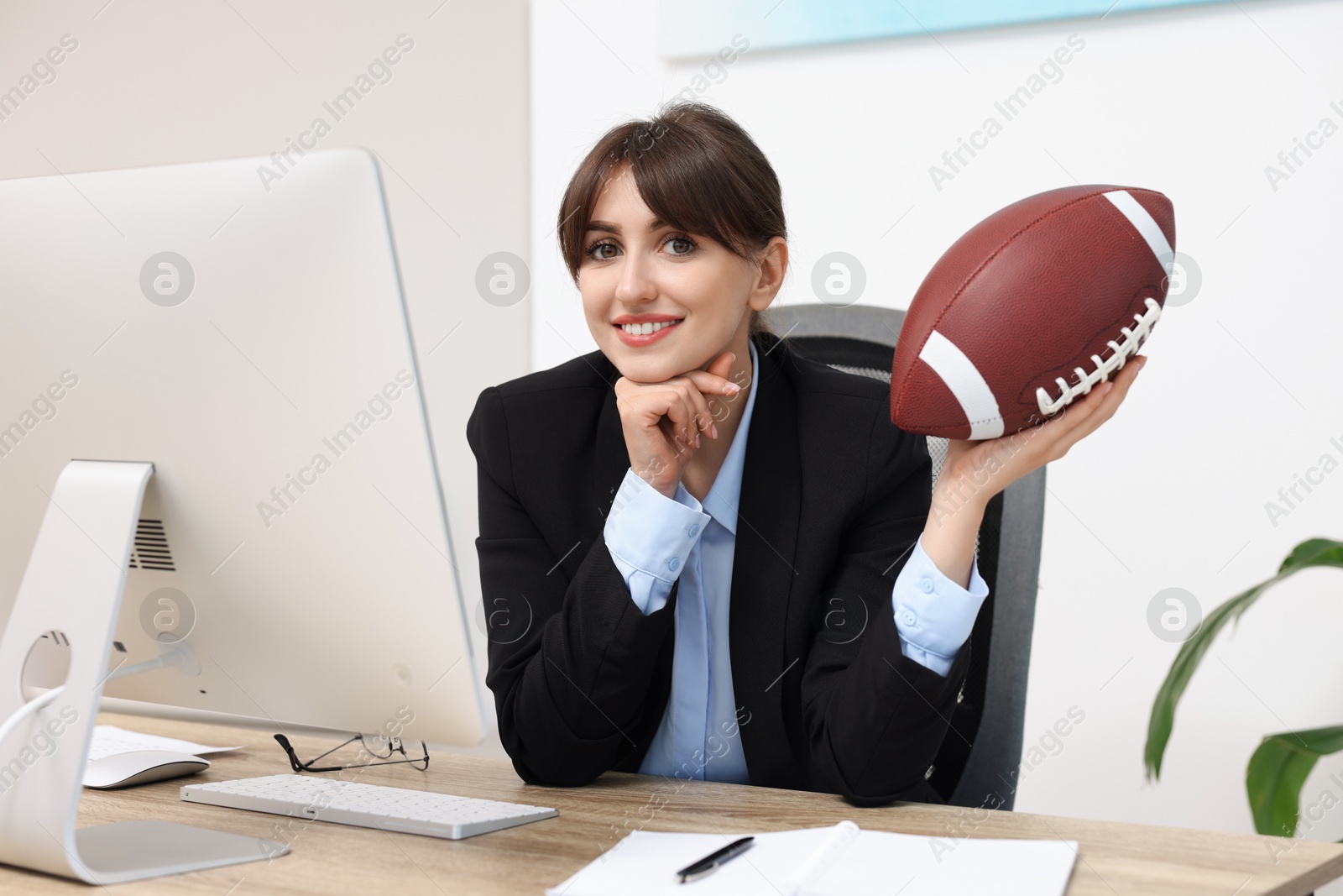 Photo of Smiling employee with american football ball at table in office