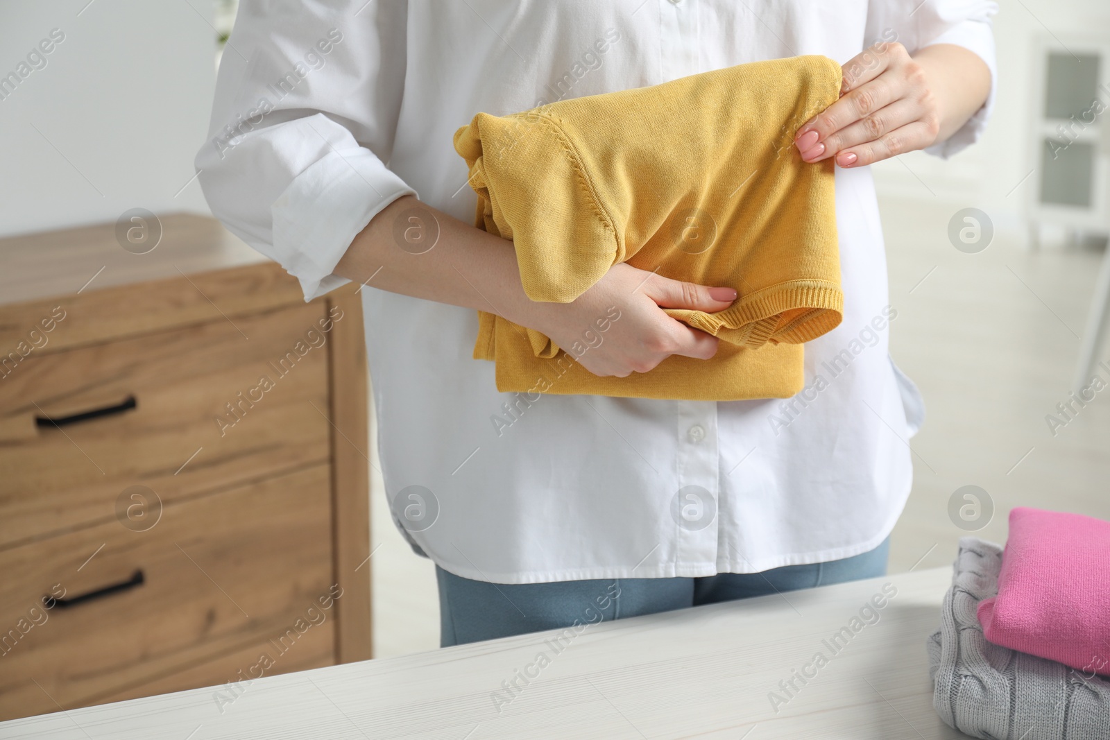 Photo of Woman folding clothes at white wooden table indoors, closeup