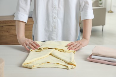 Woman folding clothes at white wooden table indoors, closeup