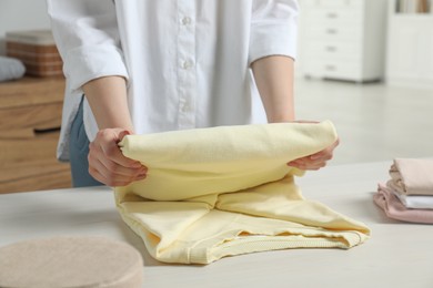 Photo of Woman folding clothes at white wooden table indoors, closeup