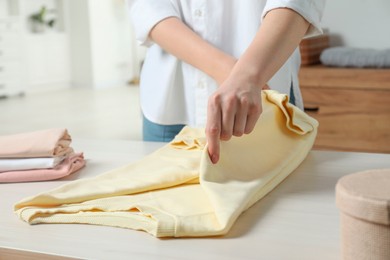 Woman folding clothes at white wooden table indoors, closeup