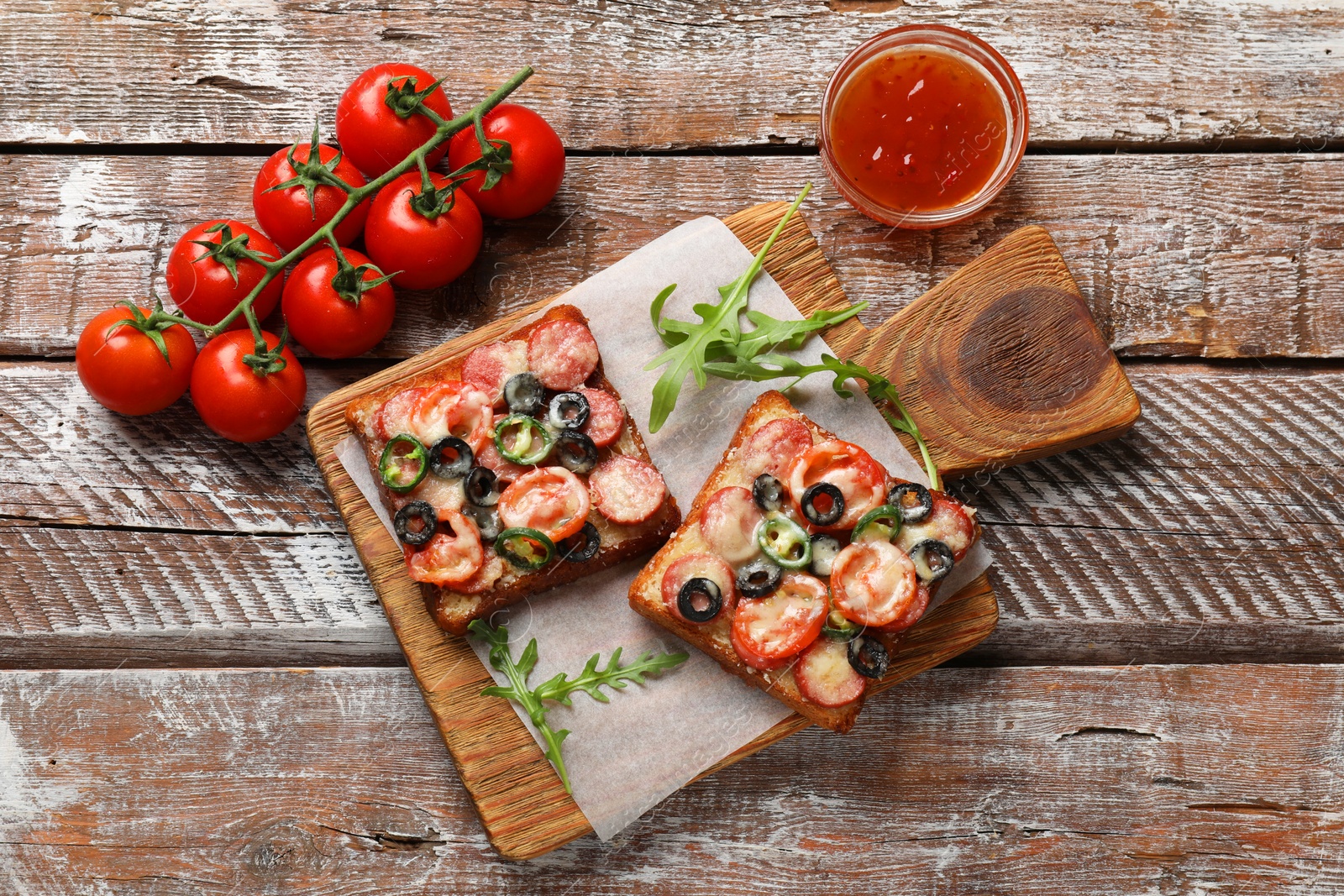 Photo of Tasty pizza toasts, sauce, tomatoes and arugula on wooden table, top view