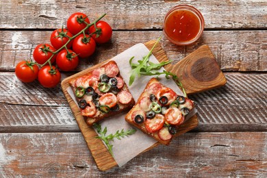 Tasty pizza toasts, sauce, tomatoes and arugula on wooden table, top view