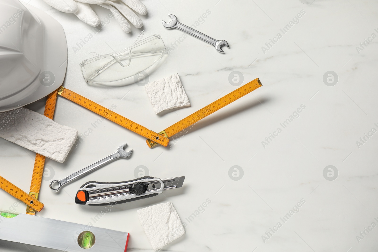 Photo of Flat lay composition with building level and other different construction tools on white marble background, space for text