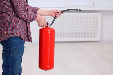 Photo of Man with fire extinguisher indoors, closeup. Space for text