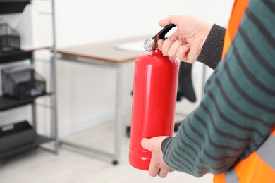 Photo of Man with fire extinguisher indoors, closeup. Space for text