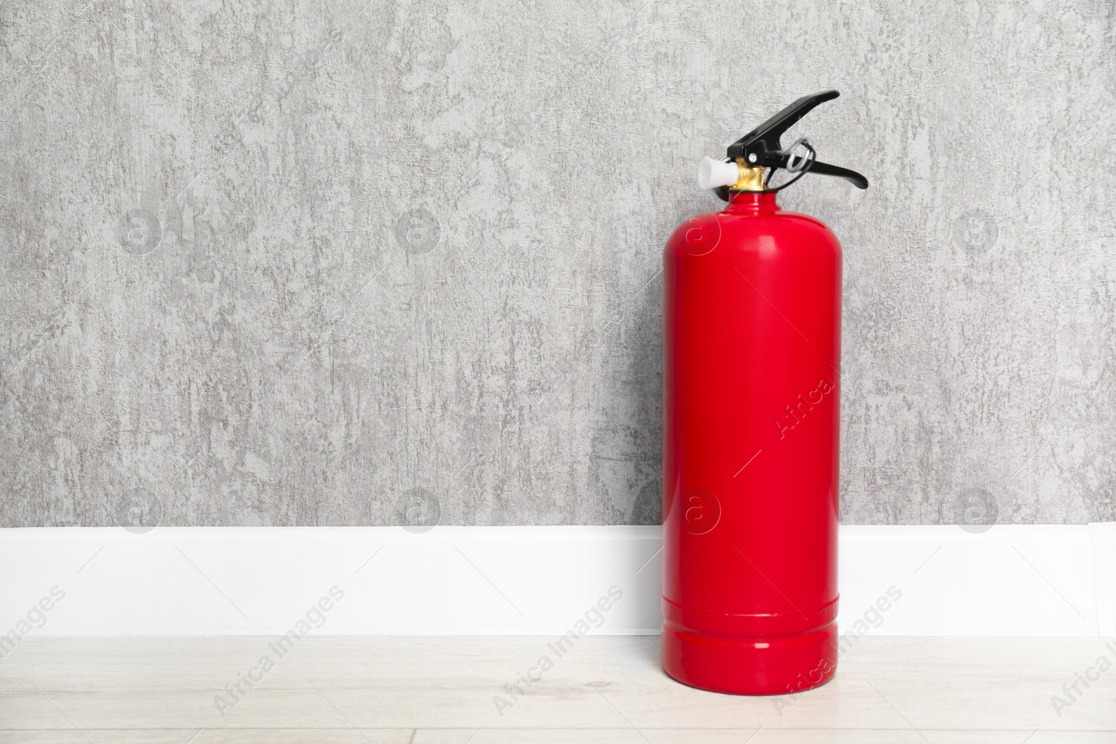 Photo of Fire extinguisher on floor near grey wall, space for text