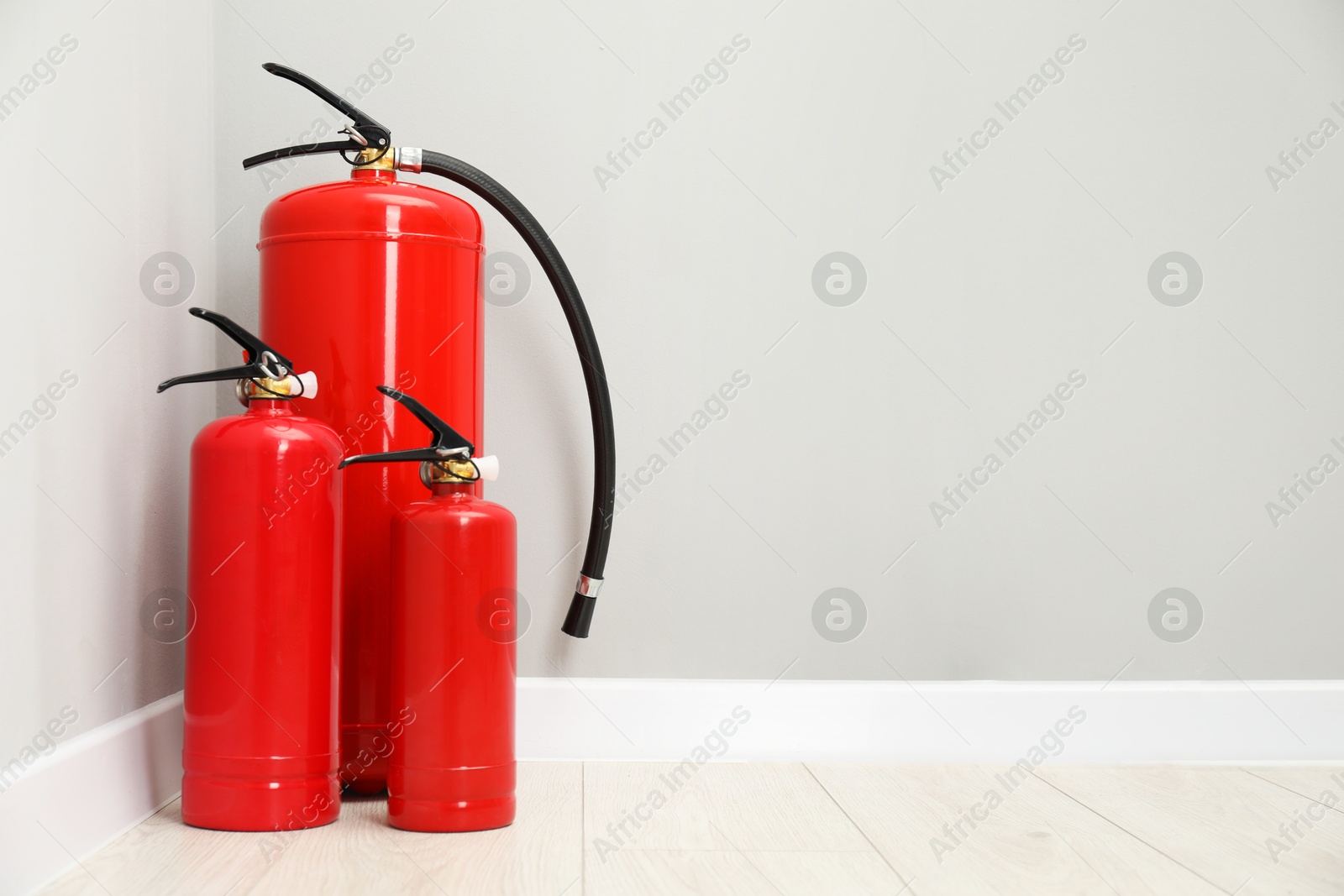 Photo of Fire extinguishers on floor near light grey wall, space for text