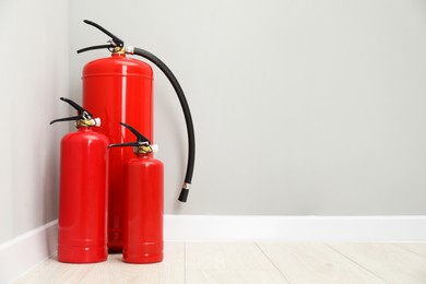 Photo of Fire extinguishers on floor near light grey wall, space for text