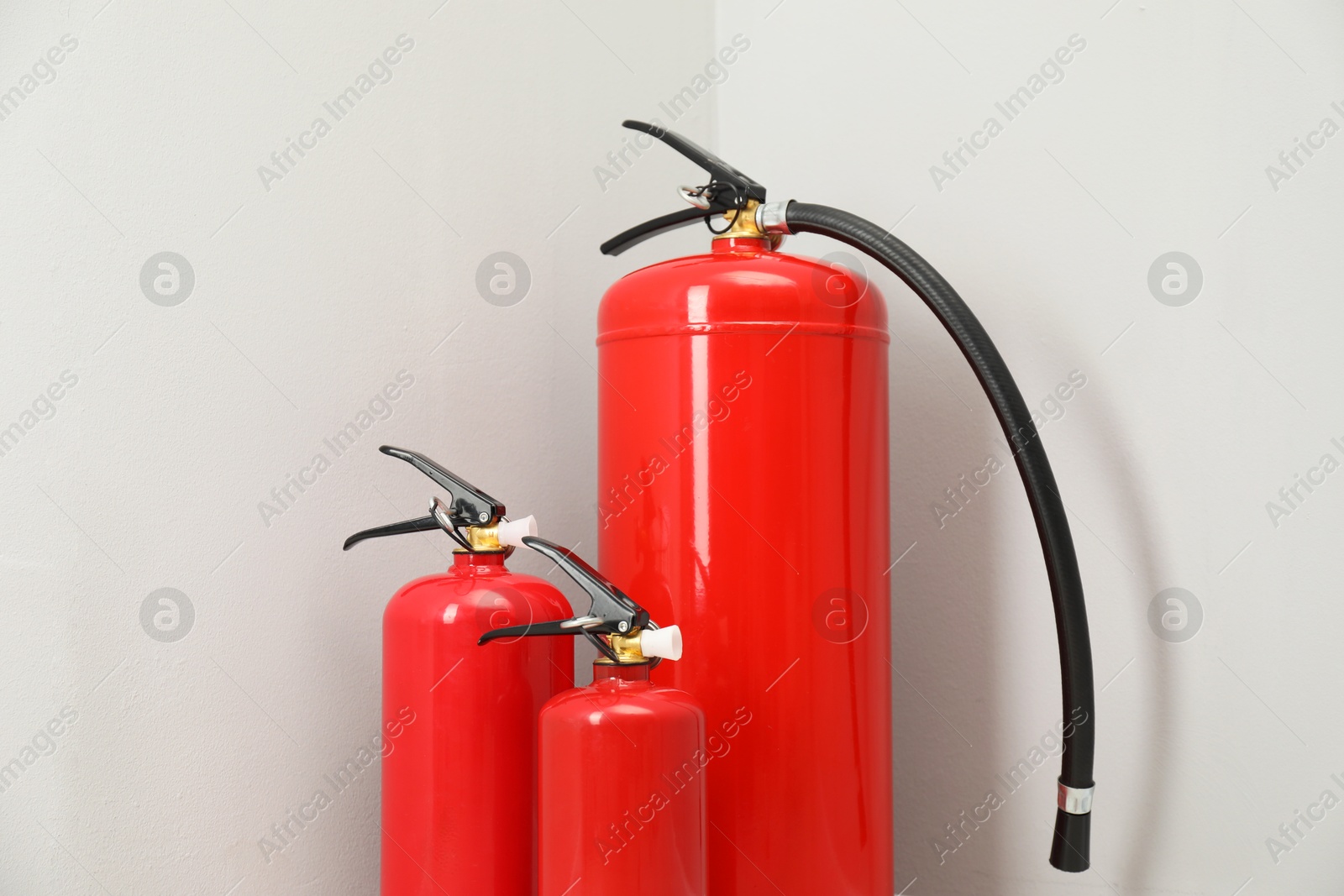 Photo of Three fire extinguishers near light grey wall