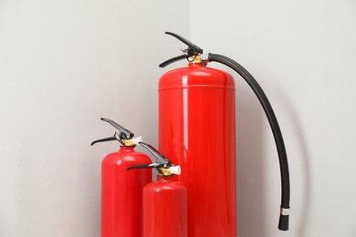 Photo of Three fire extinguishers near light grey wall