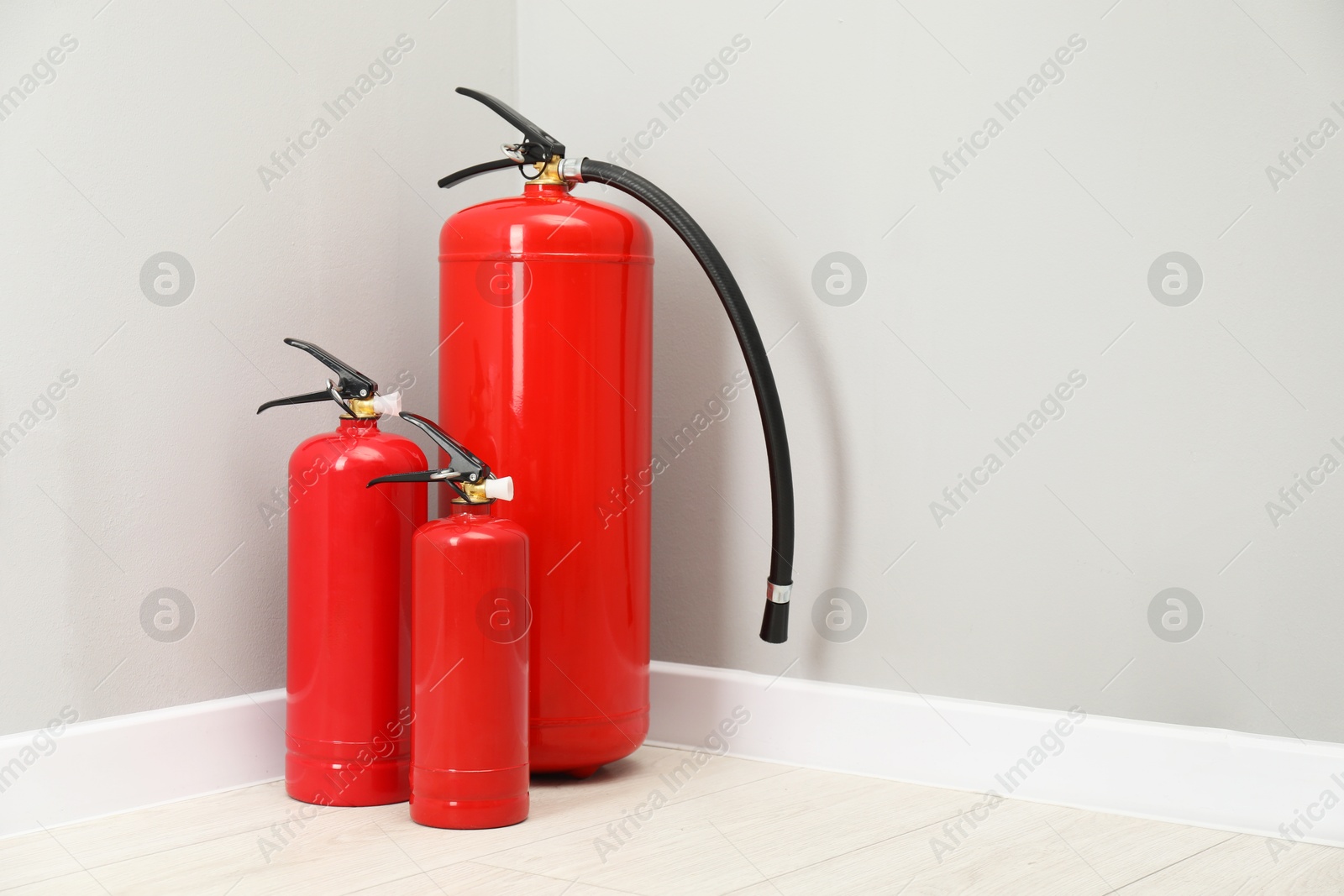 Photo of Fire extinguishers on floor near light grey wall, space for text