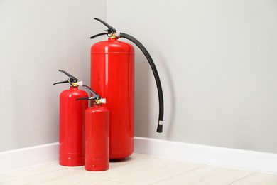 Photo of Fire extinguishers on floor near light grey wall, space for text