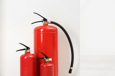 Photo of Fire extinguishers near light wall indoors, space for text