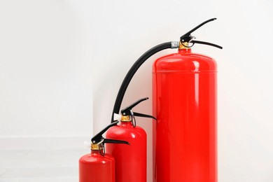 Photo of Three fire extinguishers near light wall indoors