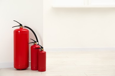 Photo of Fire extinguishers on floor near light wall indoors, space for text