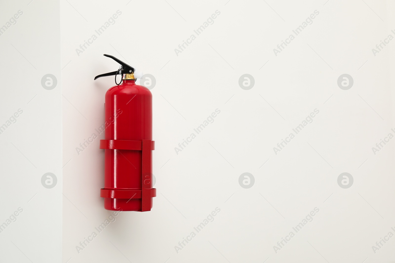 Photo of Fire extinguisher on light wall, space for text