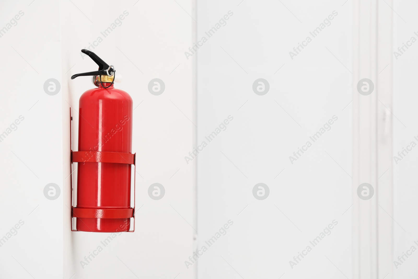 Photo of Fire extinguisher on light wall, space for text