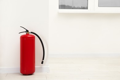 Photo of Fire extinguisher on floor near light wall indoors, space for text