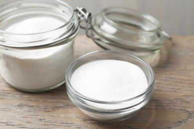 Photo of Baking soda in bowl and glass jar on wooden table, closeup