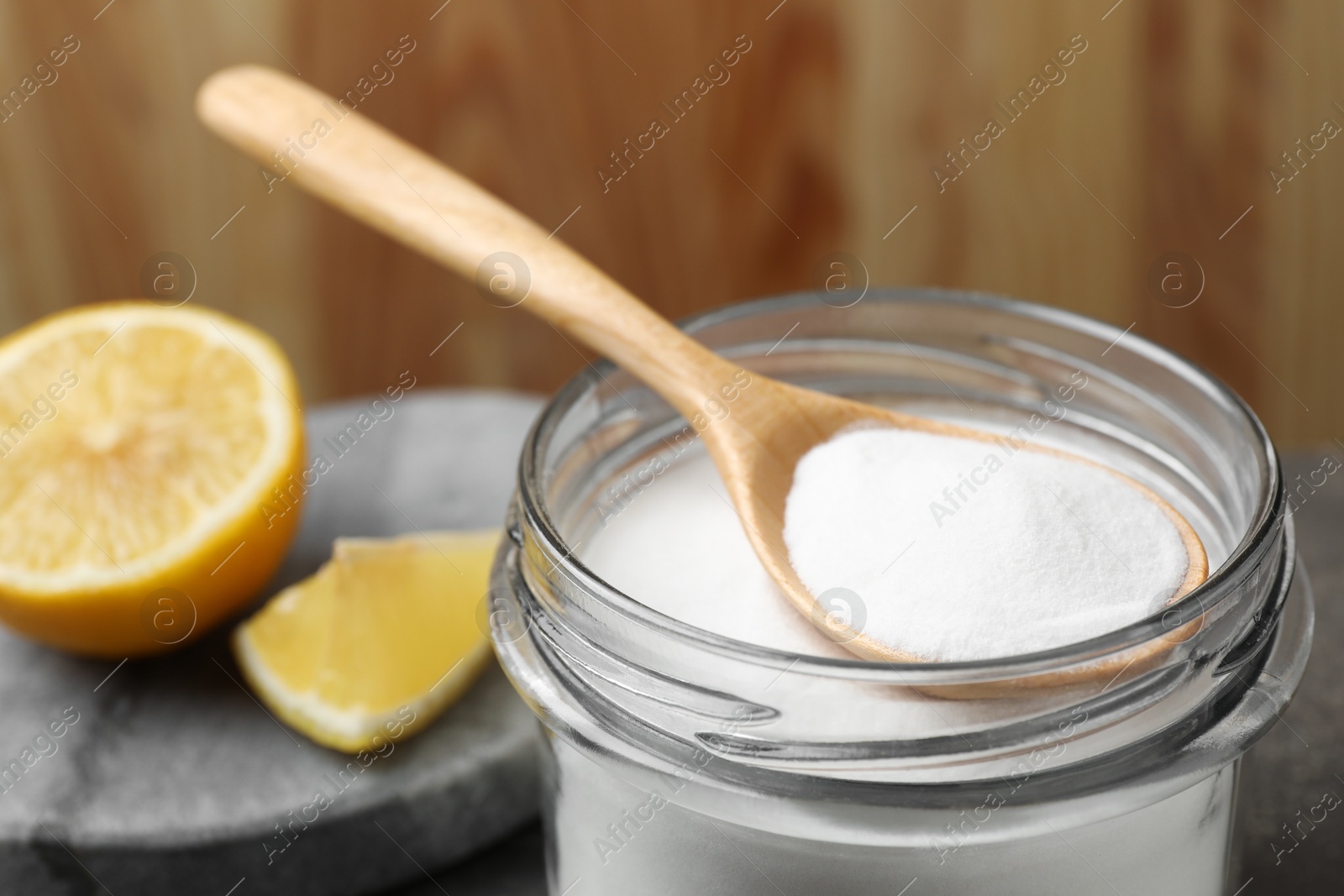 Photo of Baking soda, spoon and lemon on table, closeup