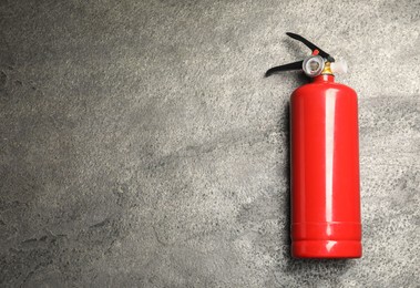 Photo of One red fire extinguisher on gray textured background, top view. Space for text