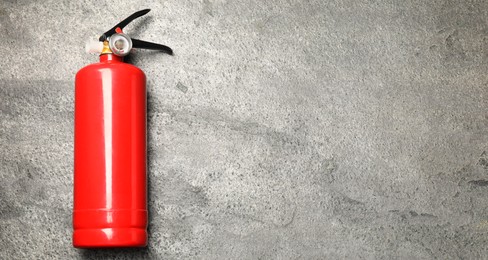 Photo of One red fire extinguisher on gray textured background, top view. Space for text