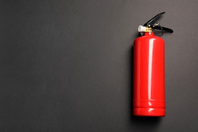 Photo of One red fire extinguisher on dark gray background, top view. Space for text