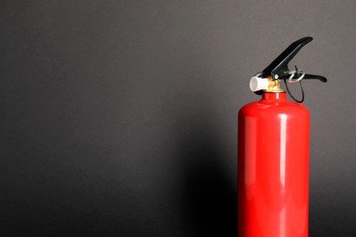 Photo of One red fire extinguisher on dark gray background, space for text