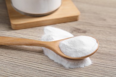 Photo of Baking soda in spoon on wooden table, closeup