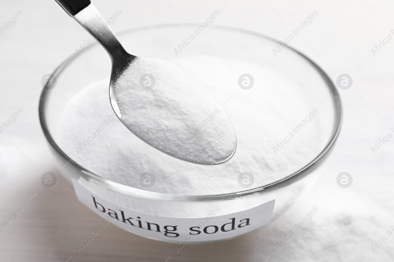 Photo of Taking baking soda from bowl at white wooden table, closeup